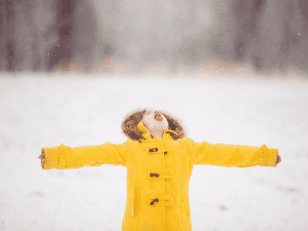 A child playing in the snow wearing a yellow winter jacket.