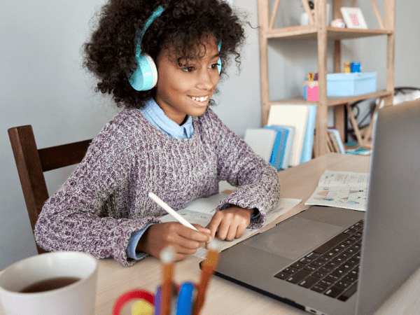 A child smiling and learning happily at her desk using a laptop and headphones.