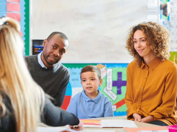 A child and his parents speaking to his teacher.